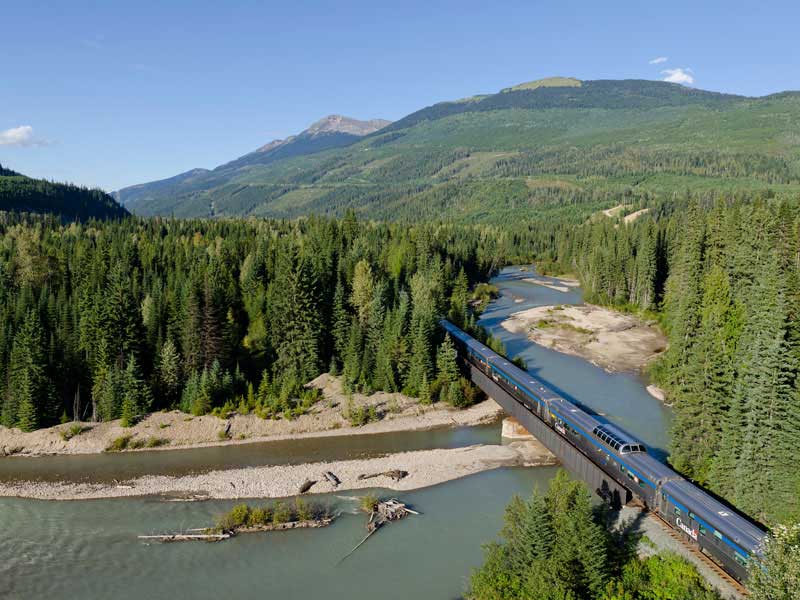 A train winding through the dense forests and mountains of the Canadian Rockies